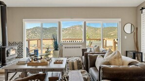 A cozy living room with a fireplace, large windows, a sofa, and a view of the mountains. - LUX Guest FAV + Stunning Views + Yoga Deck + Spa (Big Bear)