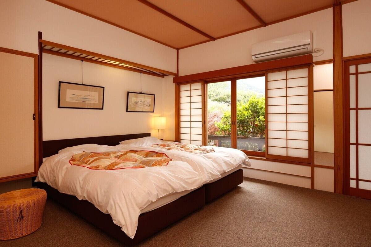 Un dormitorio de estilo japonés tradicional con suelo de tatami, futón y puertas correderas shoji, además de un equipo de aire acondicionado.