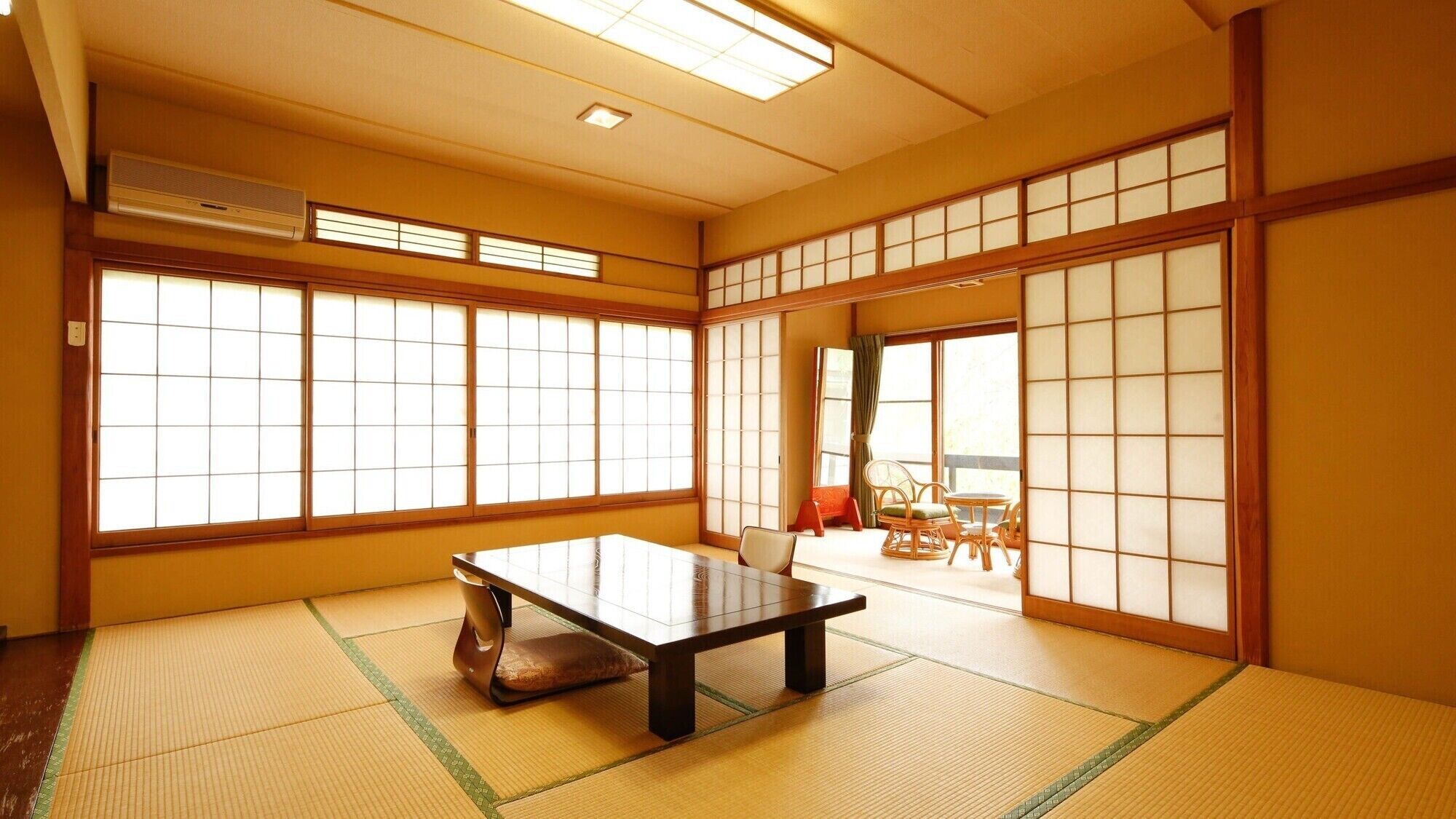 A traditional Japanese room with tatami flooring, a low table, sliding shoji doors, and a view of the outside.