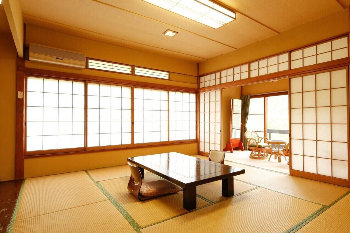Una habitación japonesa tradicional con suelo de tatami, una mesa baja, puertas correderas shoji y vistas al exterior.