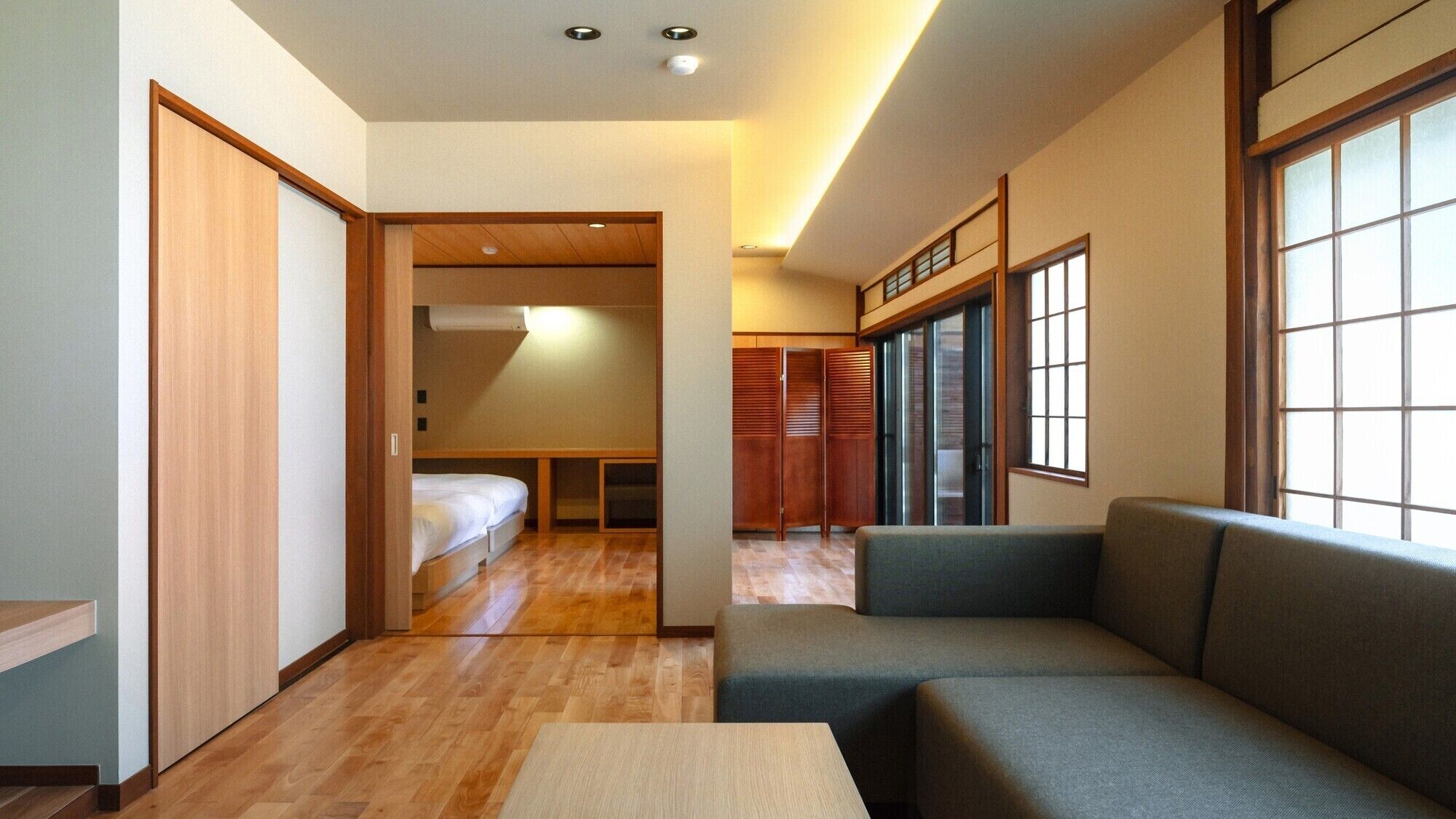 A compact hotel room with a sofa, a small table, a bed, and a wardrobe.