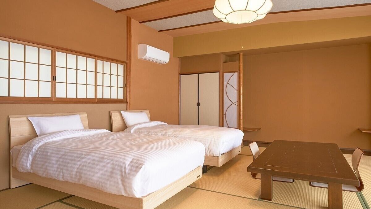 A traditional Japanese-style room with tatami flooring, two wooden beds with white bedding, a low wooden table, and sliding doors.