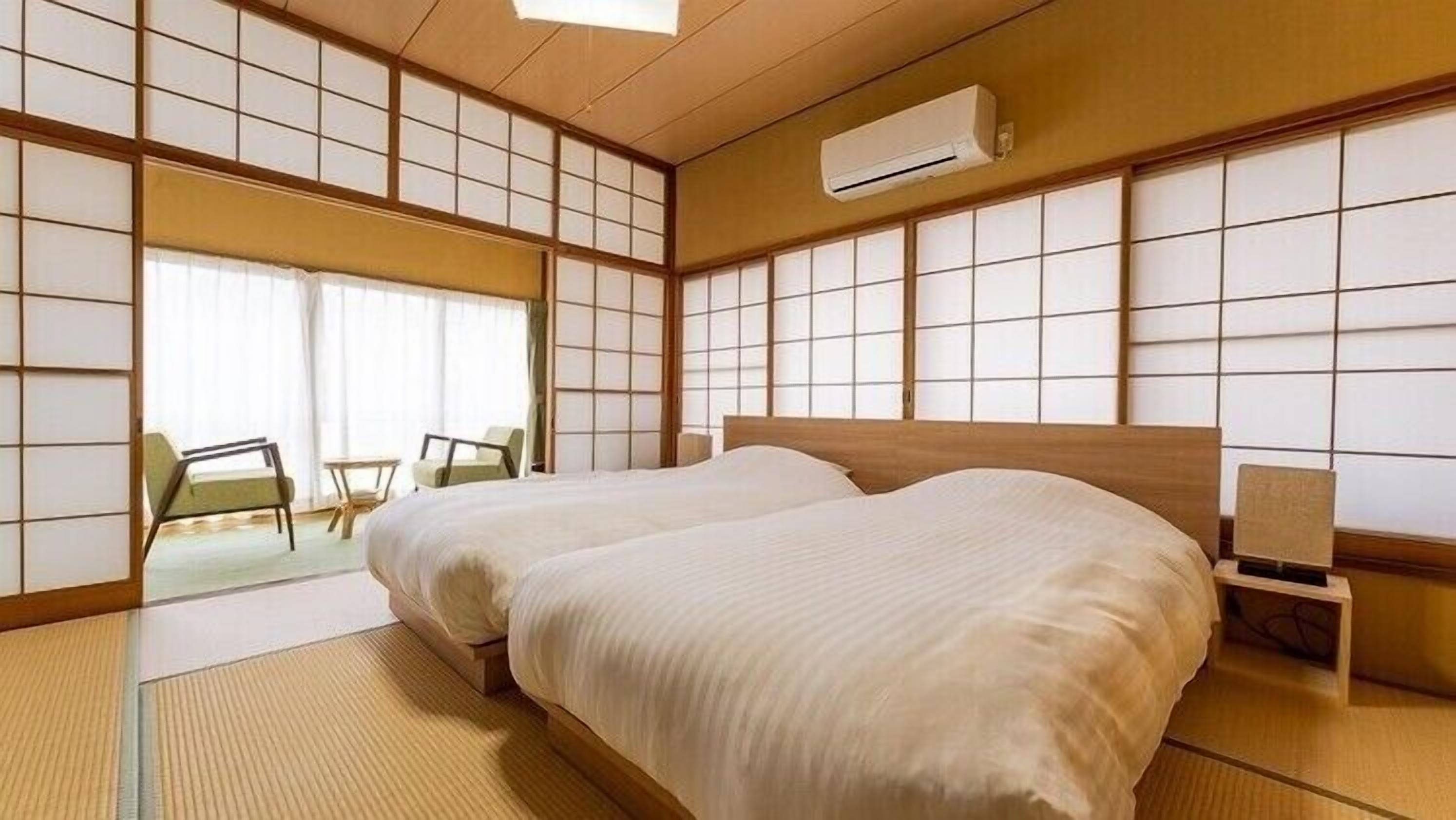 A traditional Japanese-style room with tatami flooring, a large bed, a small table, and a chair.