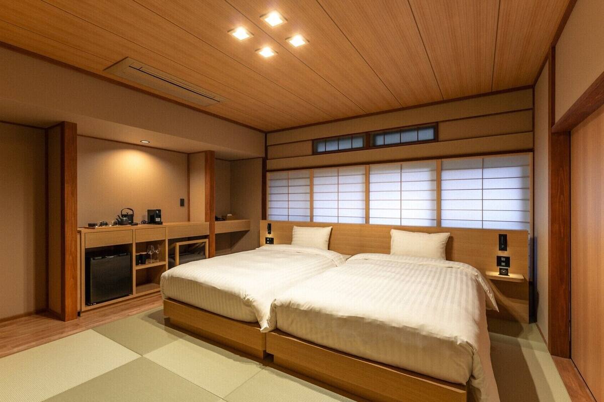 Un dormitorio tradicional japonés con cama, mesitas de noche, un escritorio y una ventana con paneles shoji.