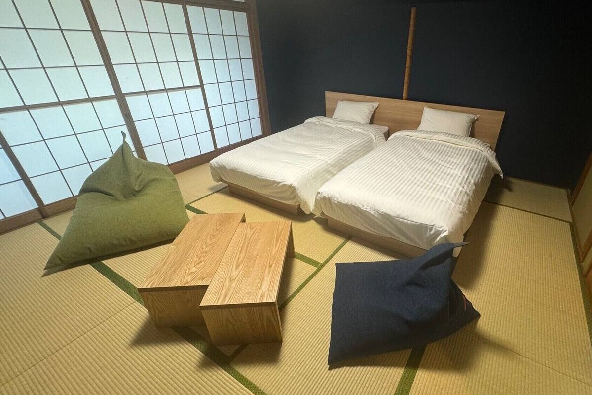 Una habitación de estilo japonés tradicional con suelo de tatami, dos camas y una mesa de madera baja.