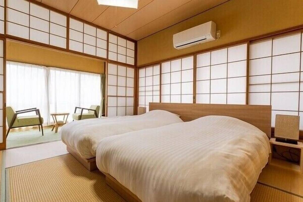 Una habitación tradicional japonesa con suelo de tatami, una cama grande, un futón, una mesita y una silla.