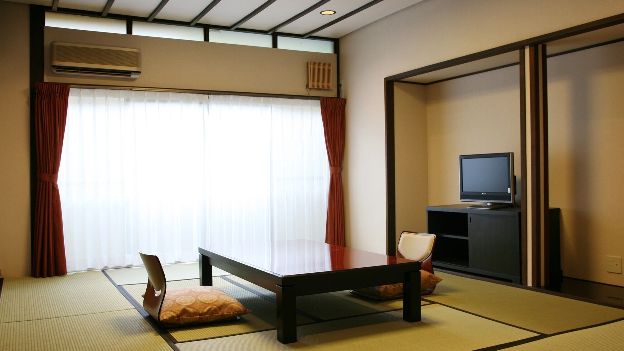 A traditional Japanese room with tatami flooring, a low table, cushions, a television, and sliding doors.
