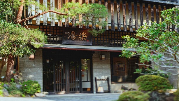 A traditional Japanese building with a wooden entrance, a sign with Japanese characters, and surrounding greenery. - Auberge Yuraku (Yugawara)