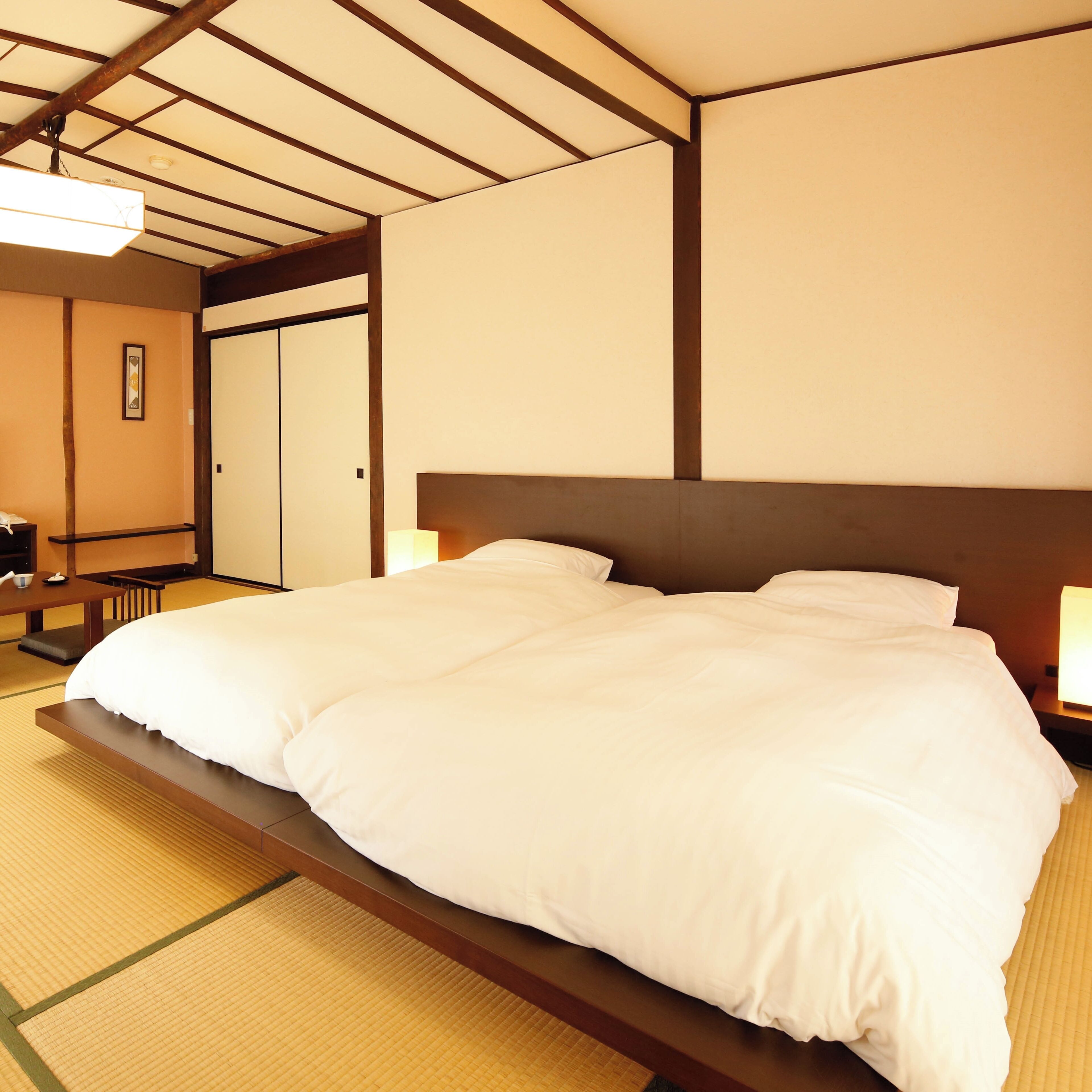 A hotel room with a bed, a nightstand, a bedside table, and a traditional Japanese tatami mat floor.