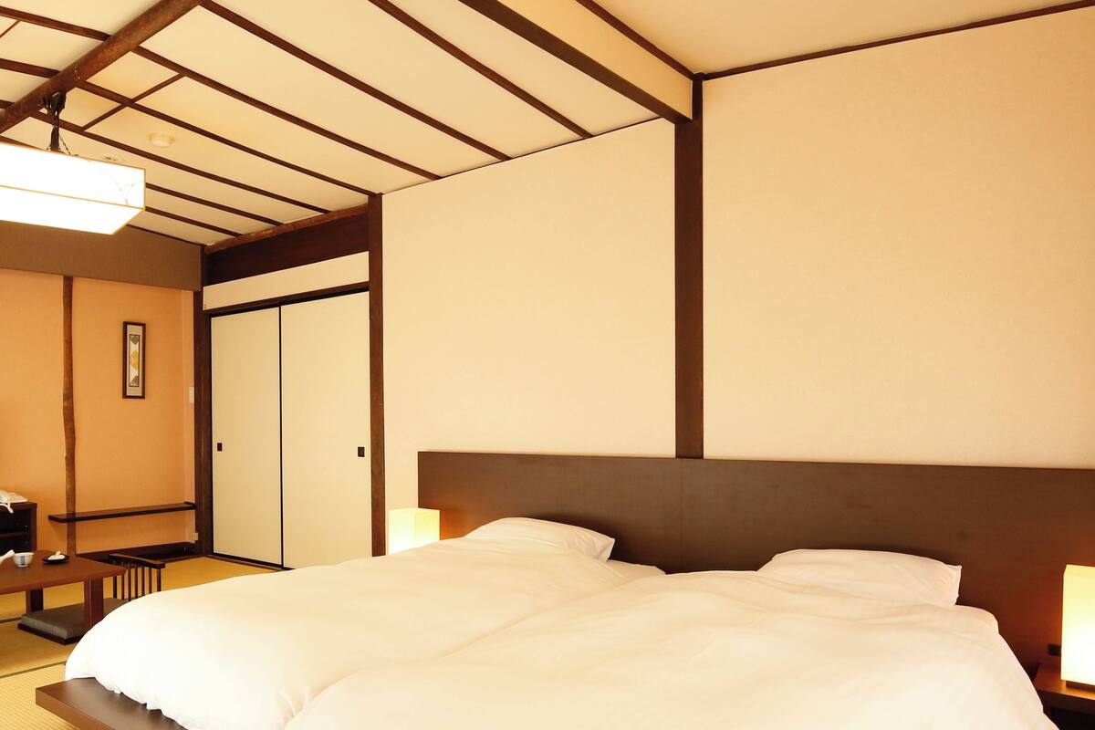 Una habitación de hotel con cama, mesita de noche y suelo tradicional de tatami japonés.