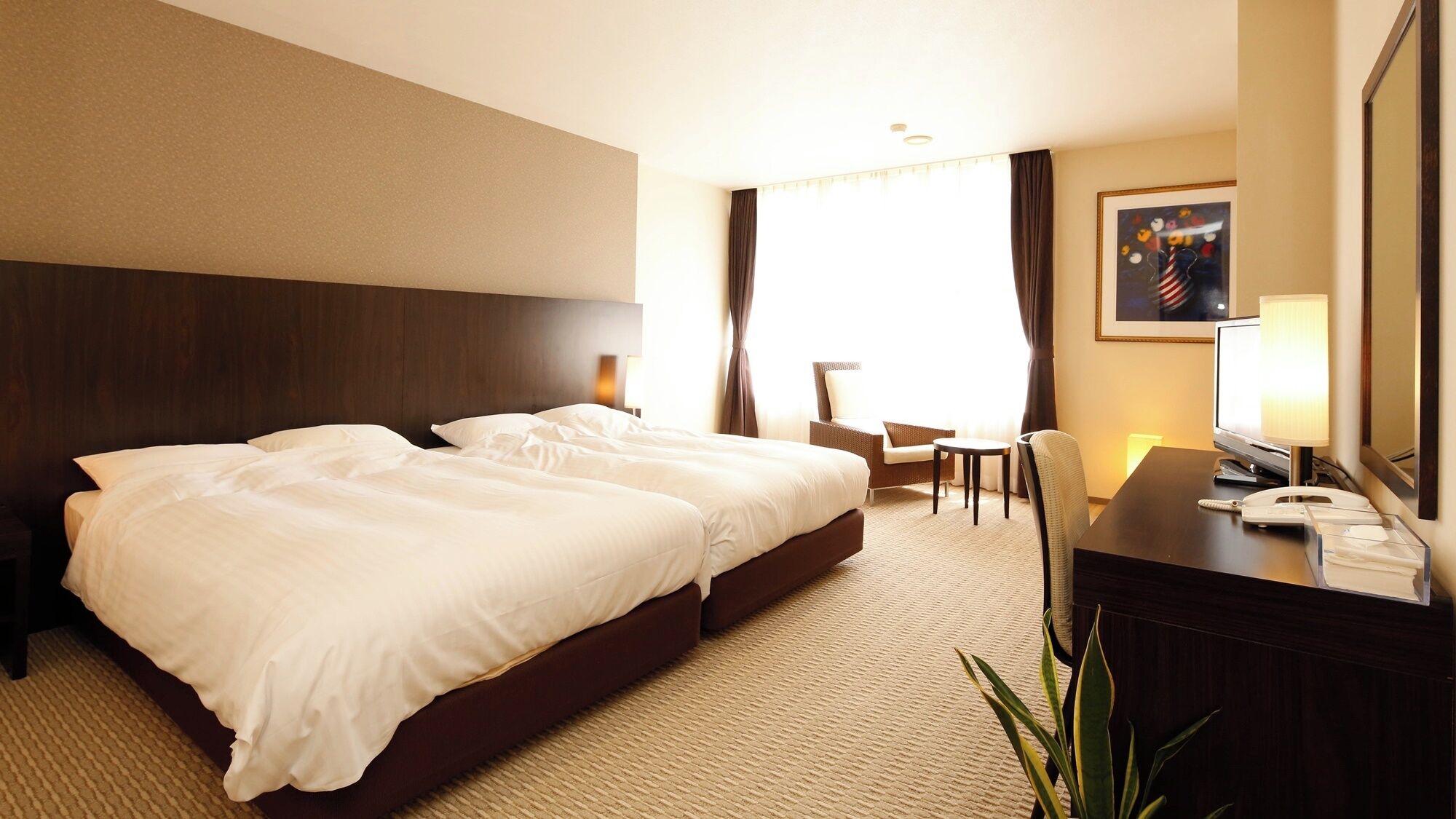 A hotel room with a large bed, a desk with a telephone, a chair, and a television.