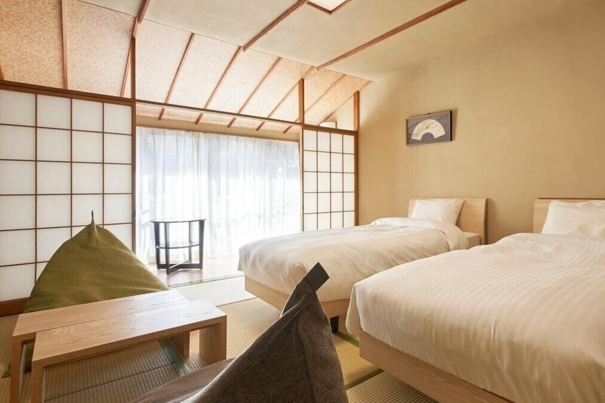 Habitación de hotel con dos camas, una mesa con tapete de tatami y un divisor corredizo estilo shoji.