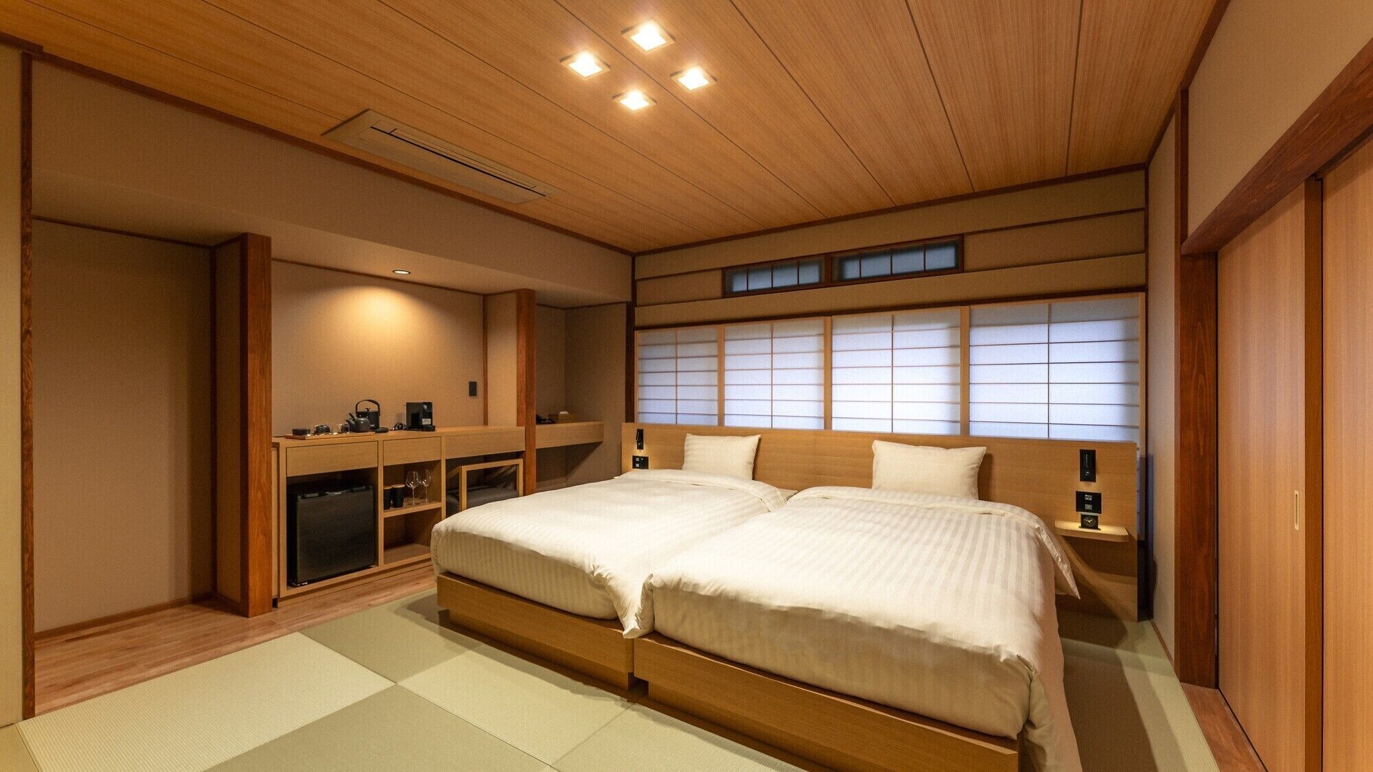 A traditional Japanese-style bedroom with a wooden ceiling, tatami flooring, a double bed, a desk with a chair, and sliding shoji doors.