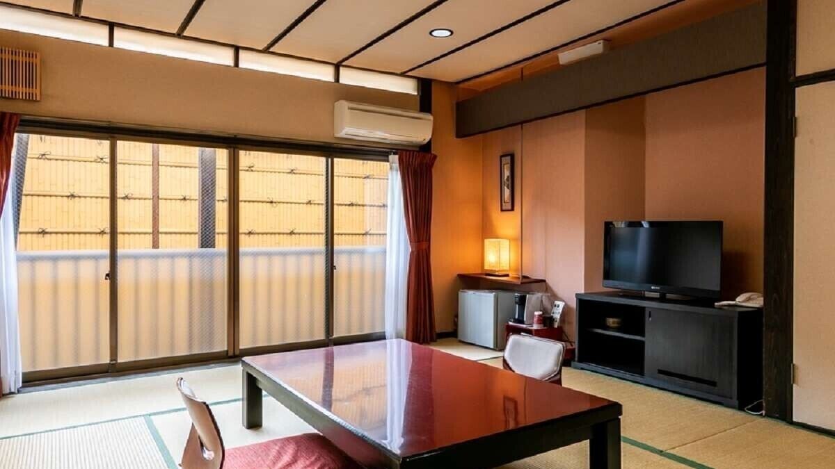 A traditional Japanese room with tatami flooring, a sliding door, a television, and a small table with a chair.