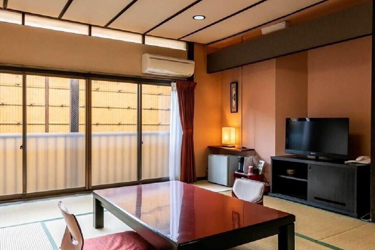 Una habitación tradicional japonesa con suelo de tatami, una puerta corredera, un televisor y una pequeña mesa con una silla.