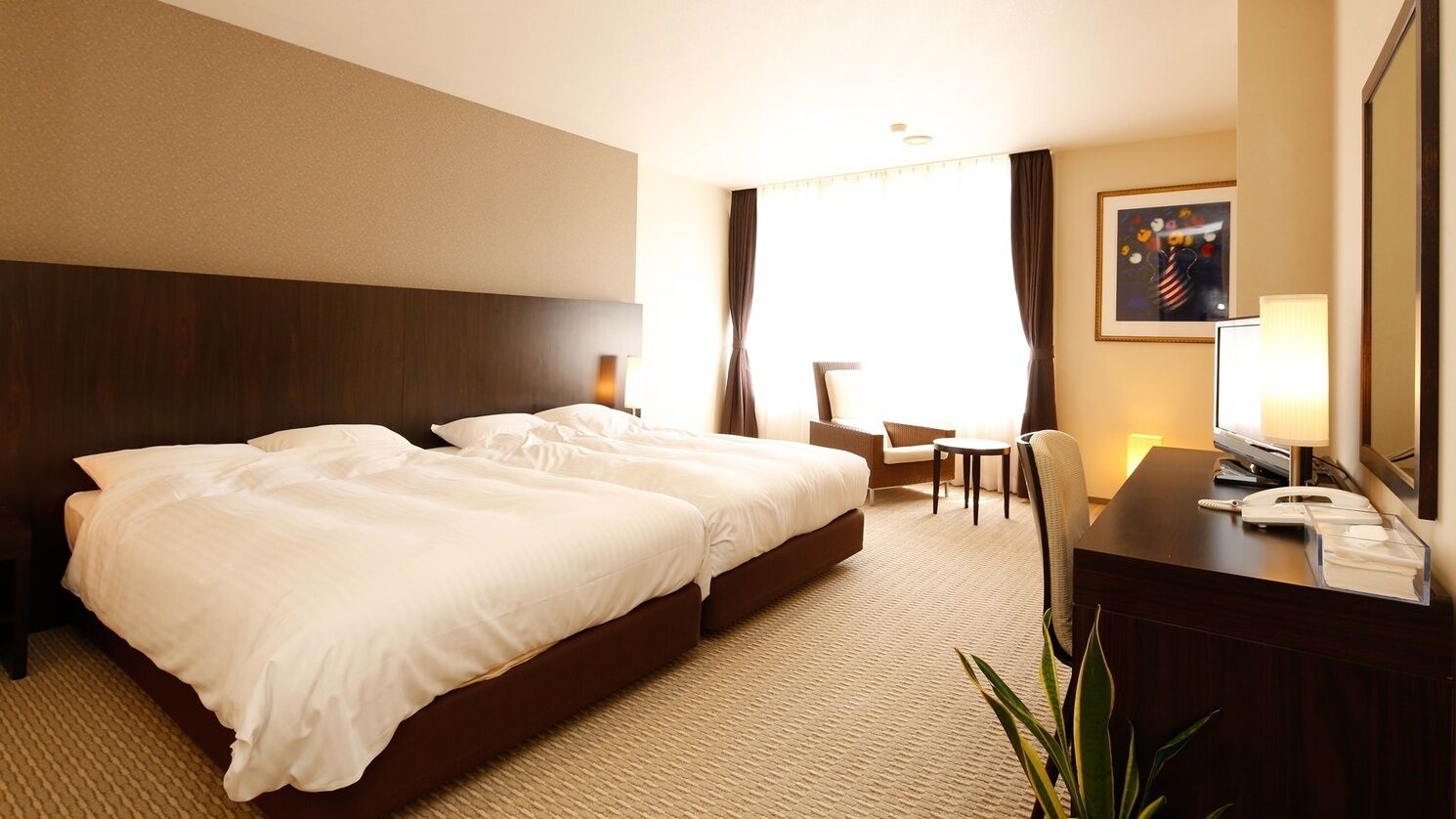 A hotel room with a large bed, a desk with a telephone, a chair, and a small table.