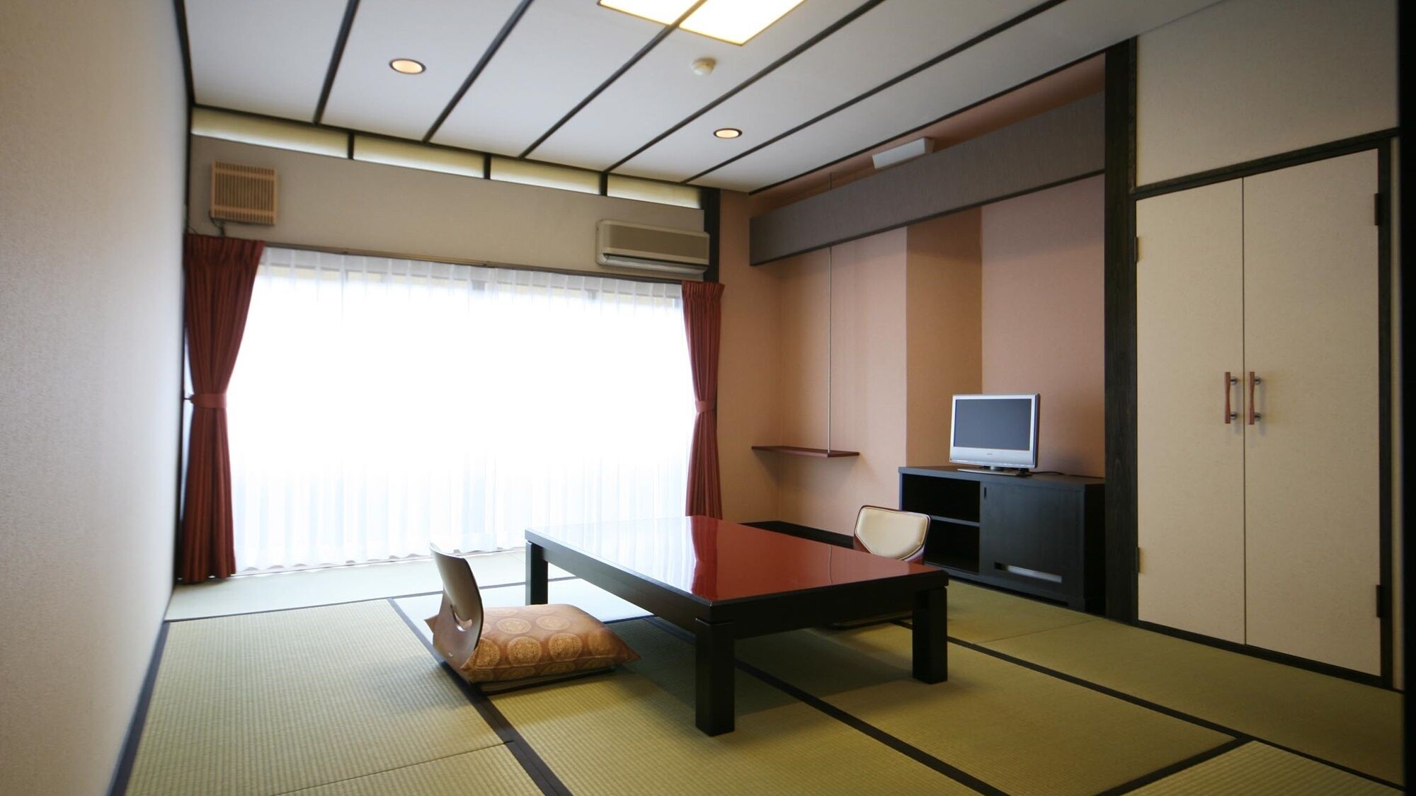 A room with tatami flooring, a low table, a sofa, a television on a cabinet, and a sliding door.