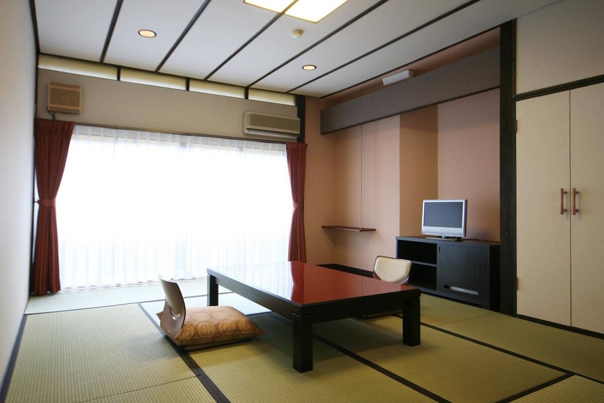 Una habitación con suelo de tatami, una mesa baja, un sofá, un televisor sobre un mueble y una puerta corredera.