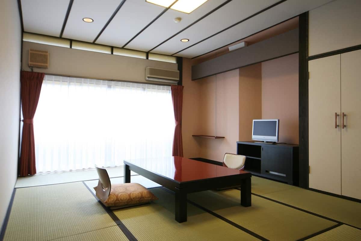 A room with tatami flooring, a low table, a sofa, a television on a cabinet, and a sliding door.
