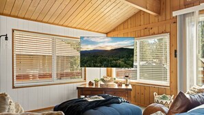 Ein gemütliches Zimmer mit Holzwänden und -decken, einem großen Flachbildfernseher an der Wand, einem Holztisch mit Lampe und einem bequemen Sofa.