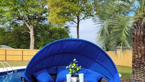 A round outdoor seating area with blue cushions and a red towel, near a pool.