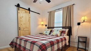 A bedroom with a wooden bed, plaid bedding, a ceiling fan, and two wall-mounted lamps.