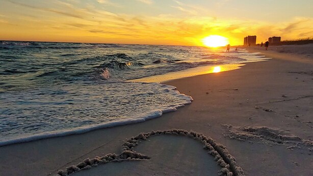 A beach with a heart-shaped sand drawing and waves at sunset.