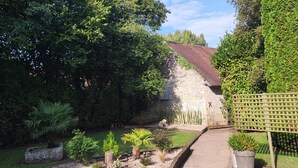 A gravel driveway leading to a stone building with a tiled roof, surrounded by lush greenery and a wooden fence. - Magnificent farmhouse on an estate 5 minutes from Caen town center (LOUVIGNY)