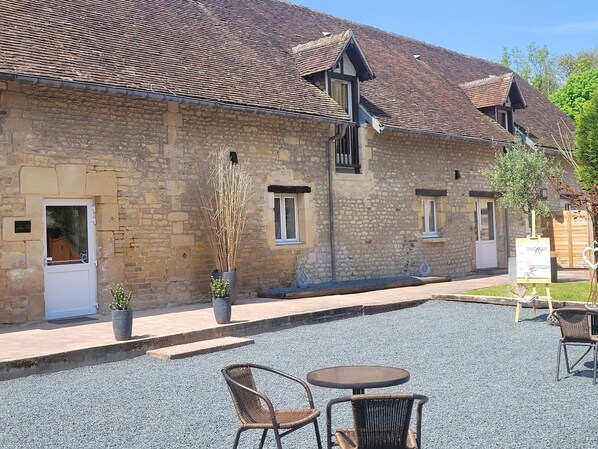 A stone building with a tiled roof, a gravel courtyard, and outdoor seating. - Magnificent farmhouse on an estate 5 minutes from Caen town center (LOUVIGNY)