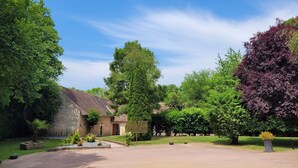 A stone building with a tiled roof, surrounded by lush greenery and trees. - Magnificent farmhouse on an estate 5 minutes from Caen town center (LOUVIGNY)