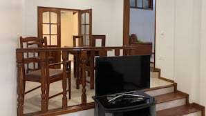 Un comedor con una mesa y sillas de madera, un televisor sobre un mueble bajo, y una escalera que sube a otra habitación.