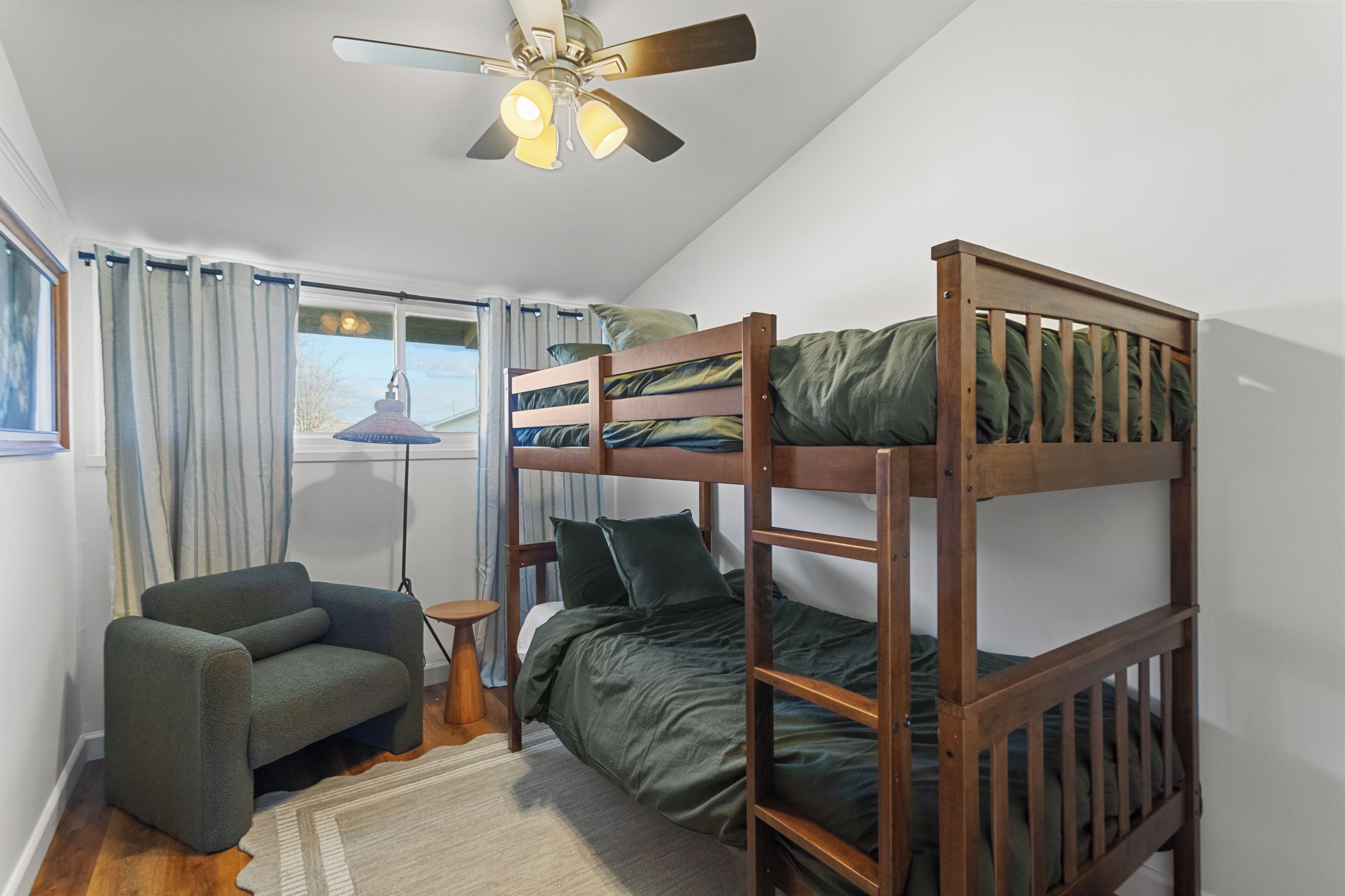 A bunk bed room with a ceiling fan, a chair, and a lamp.