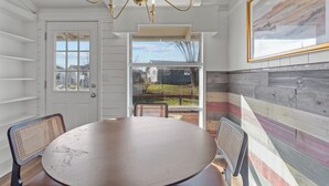 Een eetgedeelte met een ronde tafel en twee stoelen, een kroonluchter, een deur met uitzicht en een kleurrijke houten wand.