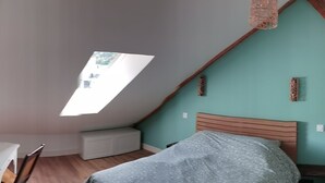 A bedroom with a sloped ceiling, a bed, a nightstand, and a window.