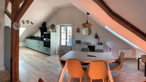 A modern loft with a dining area, kitchen, and a large window providing natural light.