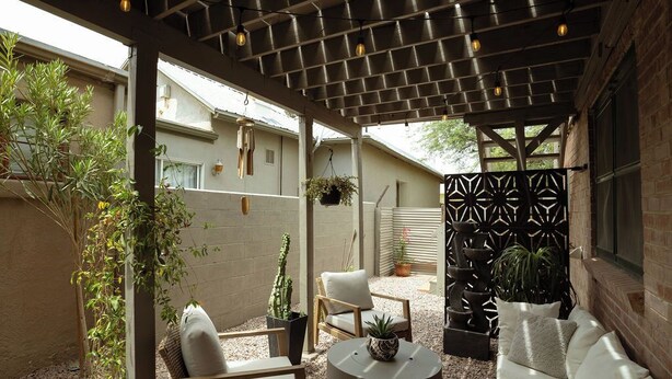 Un patio couvert aménagé avec des sièges, des plantes et une clôture décorative.