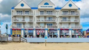 A beachfront hotel named Oceans Edge with multiple balconies, a boardwalk with shops, and a sandy beach. - Oceans Edge 503 on the Boardwalk at 9th St (Ocean City)
