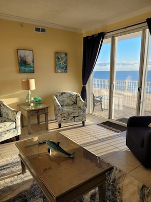 A living room with a view of the sea, a chair, a table, and a lamp.