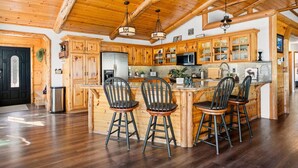 A spacious kitchen with wooden cabinets, a central island with bar stools, and a high ceiling with exposed beams.