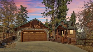 A log cabin with a stone foundation, a large garage, and a porch with a railing.