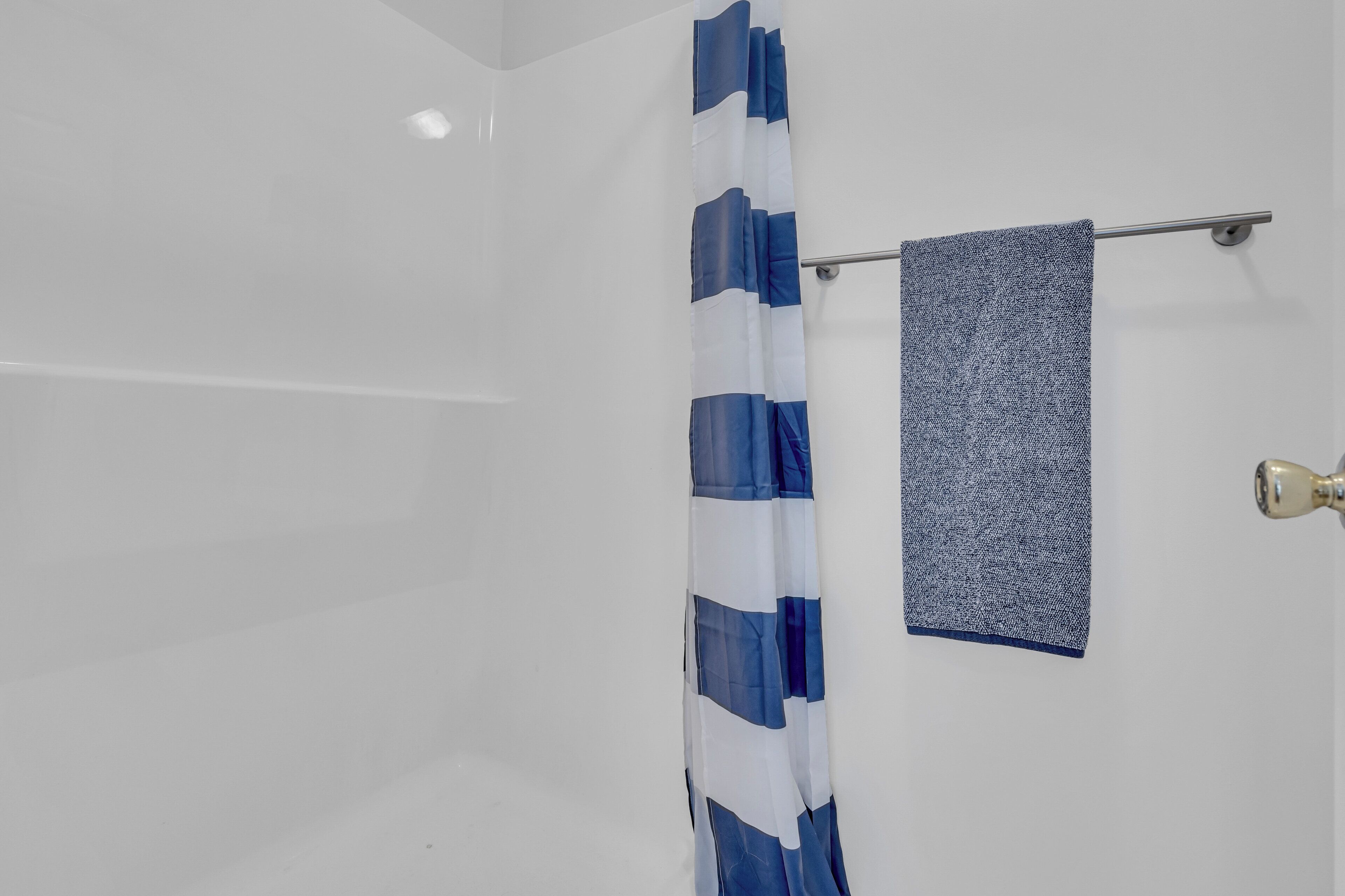 A bathroom with a white tiled wall, a blue and white striped shower curtain, and a towel hanging on a metal towel rack.