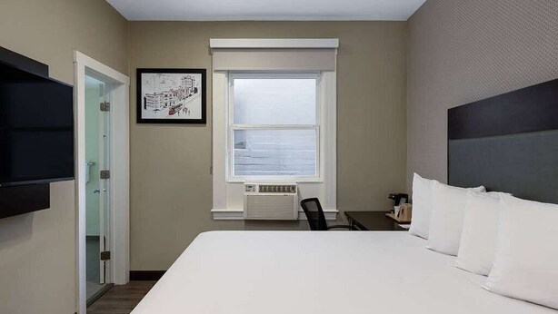 Una camera d'albergo con un letto grande, una TV a schermo piatto fissata al muro, una finestra con vista e un quadro incorniciato.
