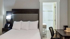 Una camera d'albergo con un letto grande, un comodino con il telefono, una scrivania con una sedia e una porta che dà su un bagno.