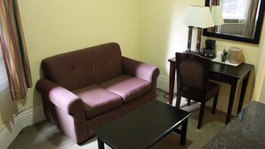 Una stanza piccola e arredata con un divano a righe, un tavolo, una sedia, una lampada e una macchina per il caffè.