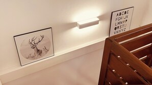 Una escalera con barandilla de madera y un estante empotrado en la pared, con obras de arte enmarcadas y una lámpara.