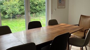 Un comedor con mesa y sillas de madera, ventanas amplias y vista a un jardín.