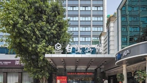 Een hotelentree met een grote boom op de voorgrond, een modern gebouw met een glazen gevel en een bord met Chinese karakters.