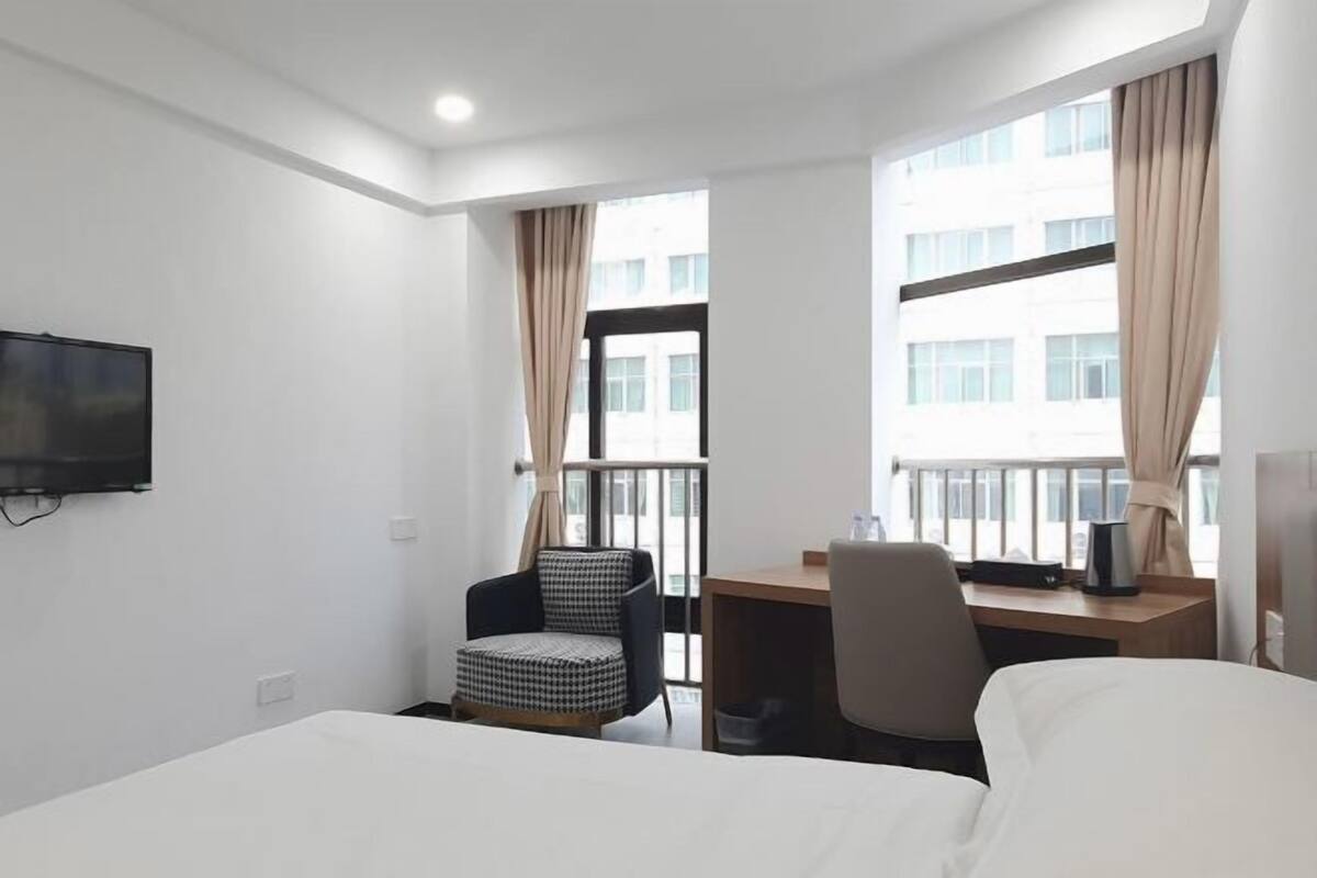 Een hotelkamer met een bed, bureau, stoel, televisie en grote ramen met gordijnen.