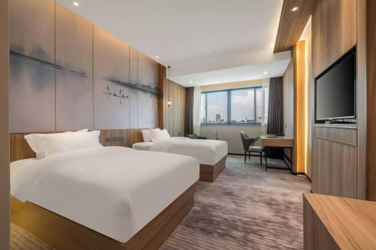 Een hotelkamer met twee bedden, een bureau, een stoel, een televisie en een groot raam met uitzicht op de stad.