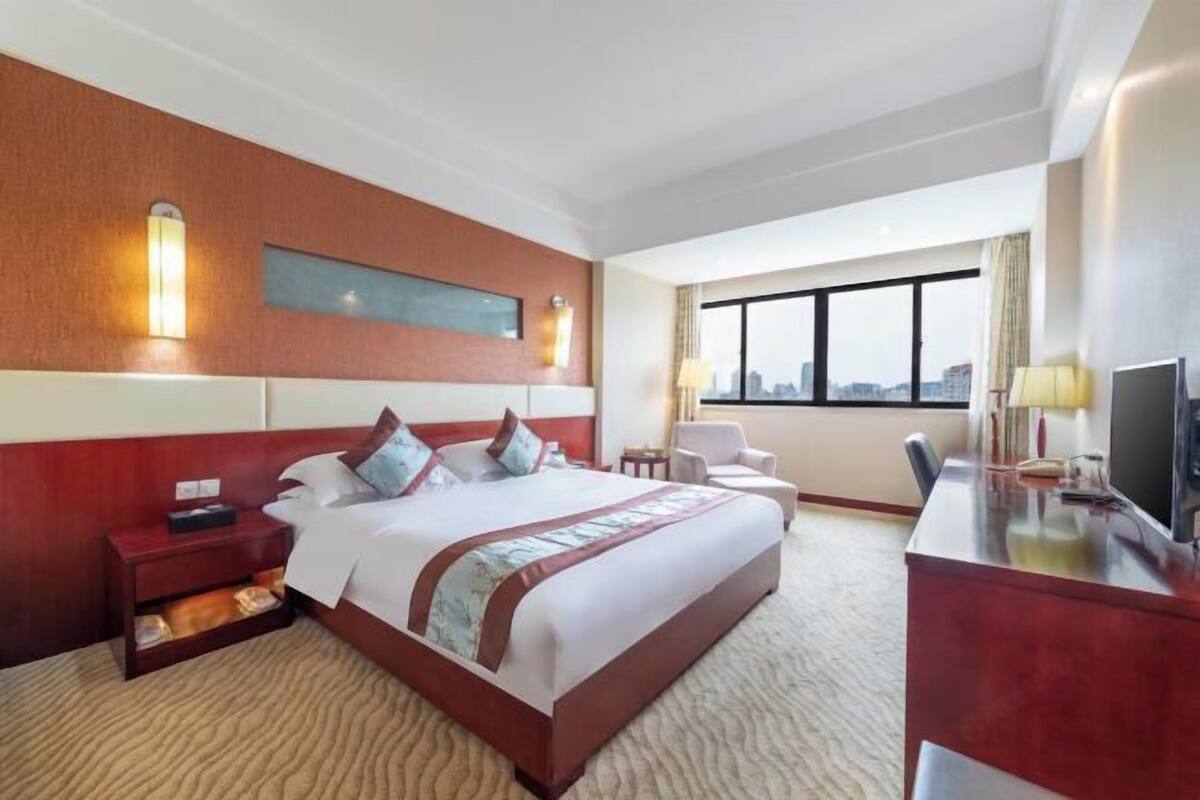 Een hotelkamer met een groot bed, een bureau, een stoel, een televisie en een raam met uitzicht op de stad.